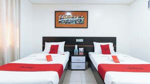 Quarto de hotel com duas camas, cada uma com roupa de cama branca e detalhes vermelhos, uma obra de arte emoldurada sobre as camas e uma pequena mesa entre elas.