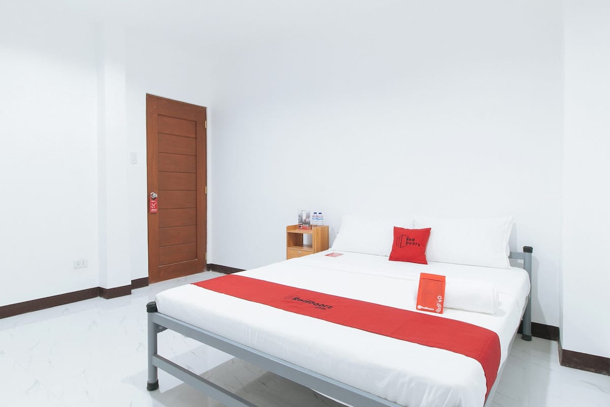 Ein Hotelzimmer mit einem Bett, einer Holztür, einem kleinen Nachttisch und einer rot-weißen Bettdecke.