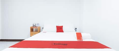 Habitación de hotel con cama, mesita de noche de madera, almohada roja y colcha roja con el logo de RedDoorz.