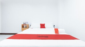 A hotel room with a bed, a wooden nightstand, a red pillow, and a red bedspread with the RedDoorz logo.