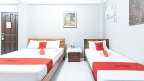 Een hotelkamer met twee bedden, elk met een rode sprei en passende kussens. Op de muur boven de bedden hangt een schilderij, en er staat een klein tafeltje met een waterfles en een boek. Er is een deur met een slot.