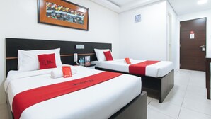 Ein Hotelzimmer mit zwei Betten, jeweils mit weißer Bettwäsche und roten Akzenten, einem Bild über den Betten, einer Uhr an der Wand und einer Tür mit einem Schild.