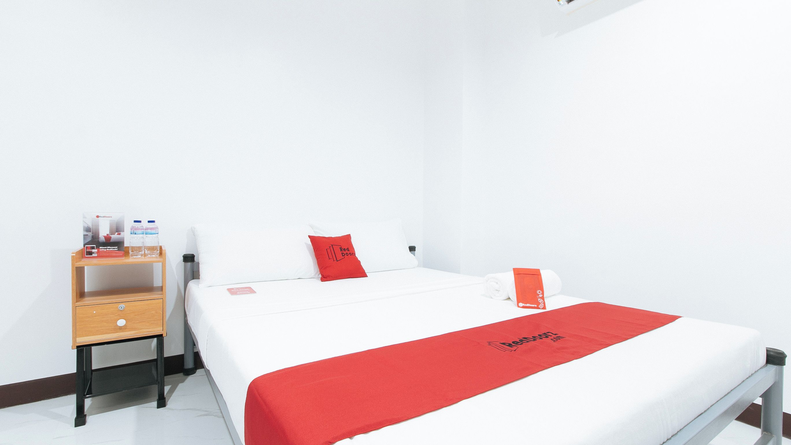 Habitación de hotel con cama, mesita de noche de madera, toalla roja y manta roja con el logotipo de Redwood.