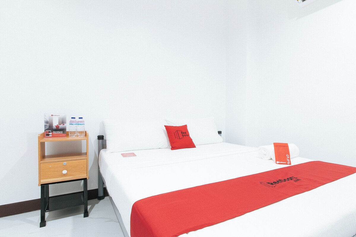 Hotelkamer met een bed, een nachtkastje van hout, een rode handdoek en een rode plaid met het Redwood logo.