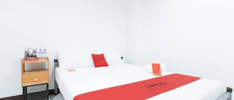 Habitación de hotel con cama, mesita de noche de madera, toalla roja y manta roja con el logotipo de Redwood.