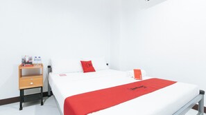 Ein Hotelzimmer mit einem Bett, einem hölzernen Nachttisch, einem roten Handtuch und einer roten Decke mit dem Redwood-Logo.