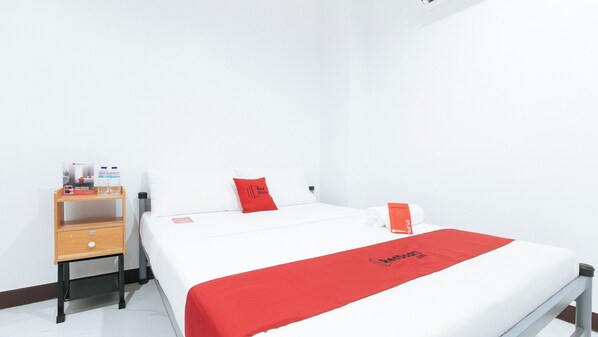 A hotel room with a bed, a wooden nightstand, a red towel, and a red blanket with the Redwood logo.