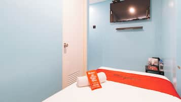A hotel room with a bed, a TV mounted on the wall, a water bottle, and a towel on the bed.