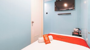Habitación de hotel con cama, televisor montado en la pared, botella de agua y toalla sobre la cama.