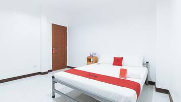 A hotel room with a bed, a wooden door, a small wooden nightstand, and a red and white bedspread.