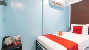 Hotelkamer met een bed, een kussen, een rode deken, een kussensloop, een nachtkastje, een waterkoker, en een RedDoorz bord.