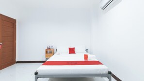 A hotel room with a bed, a wooden nightstand, a red pillow, and a white wall.