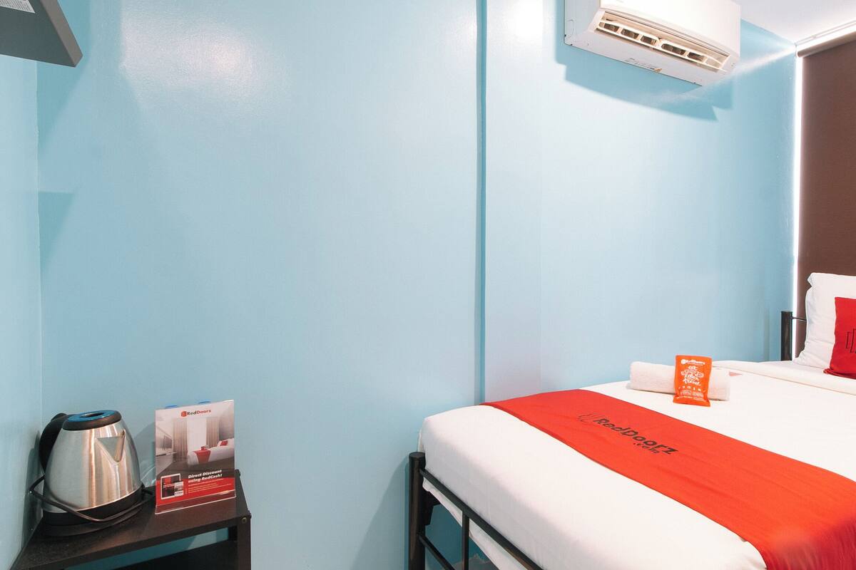 Ein Hotelzimmer mit einem Bett, einem Kissen, einer roten Decke, einem Kissenbezug, einem Nachttisch, einem Wasserkocher und einem RedDoorz Schild.
