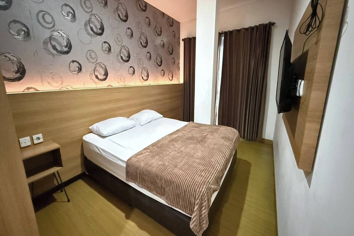 Ein Hotelzimmer mit Bett, einem Kopfschild mit kreisförmigem Muster, einem Nachttisch und einem an der Wand montierten Fernseher.