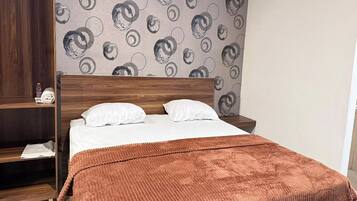 Un dormitorio con cama de madera, almohadas blancas, una manta marrón y una pared con diseño circular.