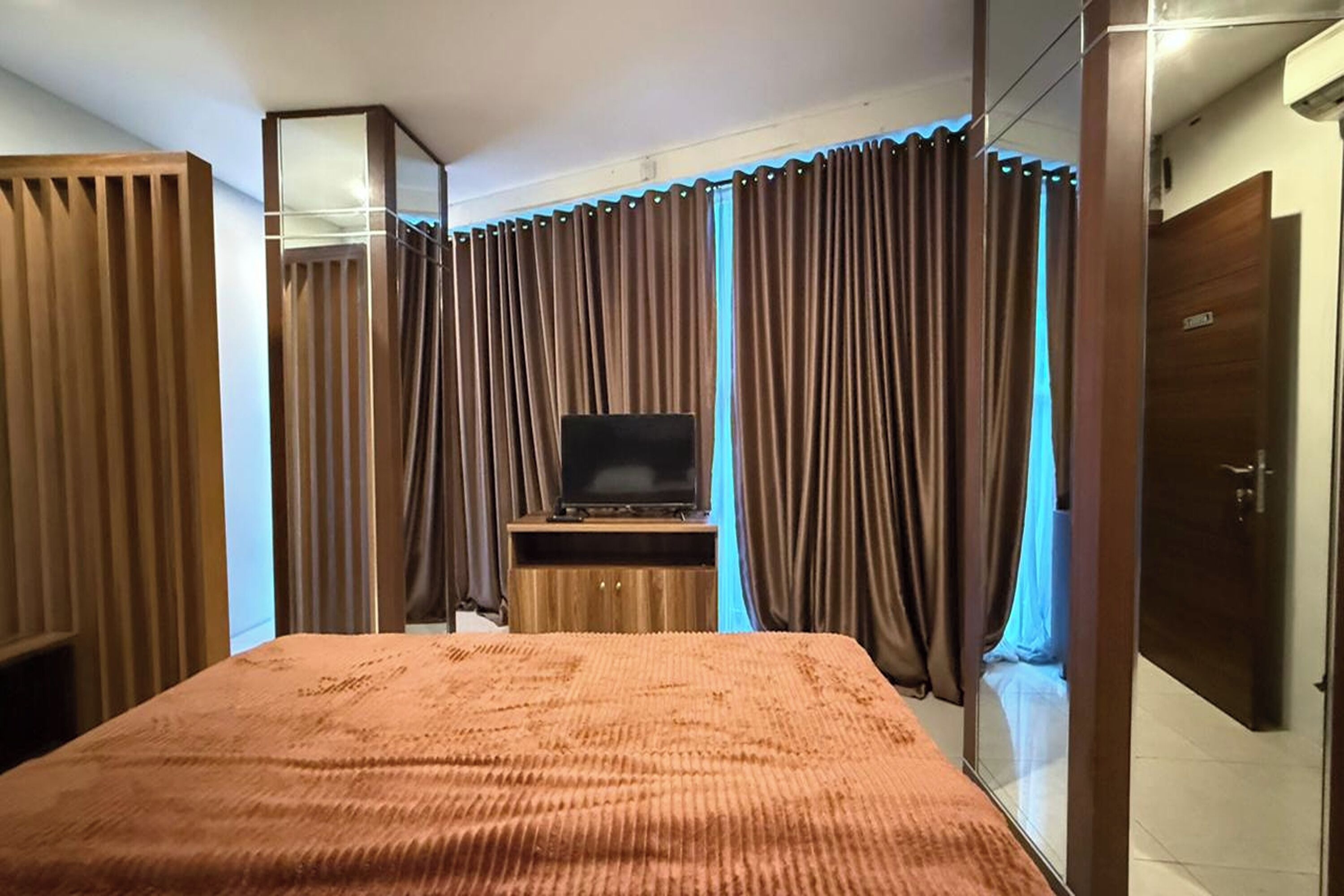 Une chambre d’hôtel avec un grand lit, un téléviseur posé sur un meuble en bois et une armoire avec un miroir.