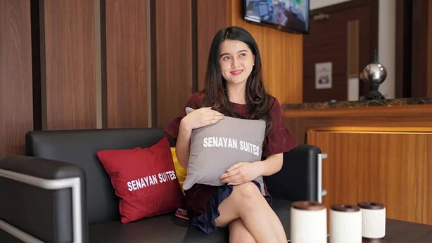 A person sitting on a black leather sofa with a red pillow labeled "SENAYAN SUITES". - Senayan Suites (Jakarta)