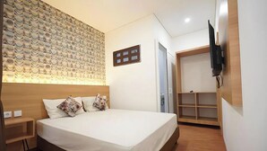A hotel room with a large bed, wooden headboard, a wall-mounted TV, and a built-in wardrobe. - Senayan Suites (Jakarta)