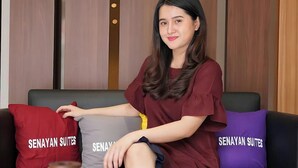 A person sitting on a sofa with three pillows labeled "SENAYAN SUITES". - Senayan Suites (Jakarta)