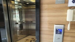 An elevator with a glass door, a wall-mounted phone, and a control panel with a directional arrow. - Senayan Suites (Jakarta)
