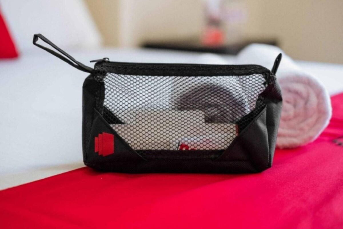 Una bolsa de malla negra con cremallera y una etiqueta roja, sobre una superficie roja.