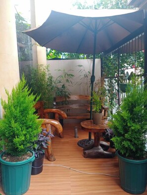 Un'area patio con mobili in legno, piante in vaso e un ombrellone grande.