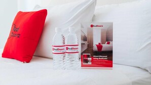 Un lit avec un oreiller rouge, deux bouteilles d’eau RedDoorz et une boîte promotionnelle RedDoorz.