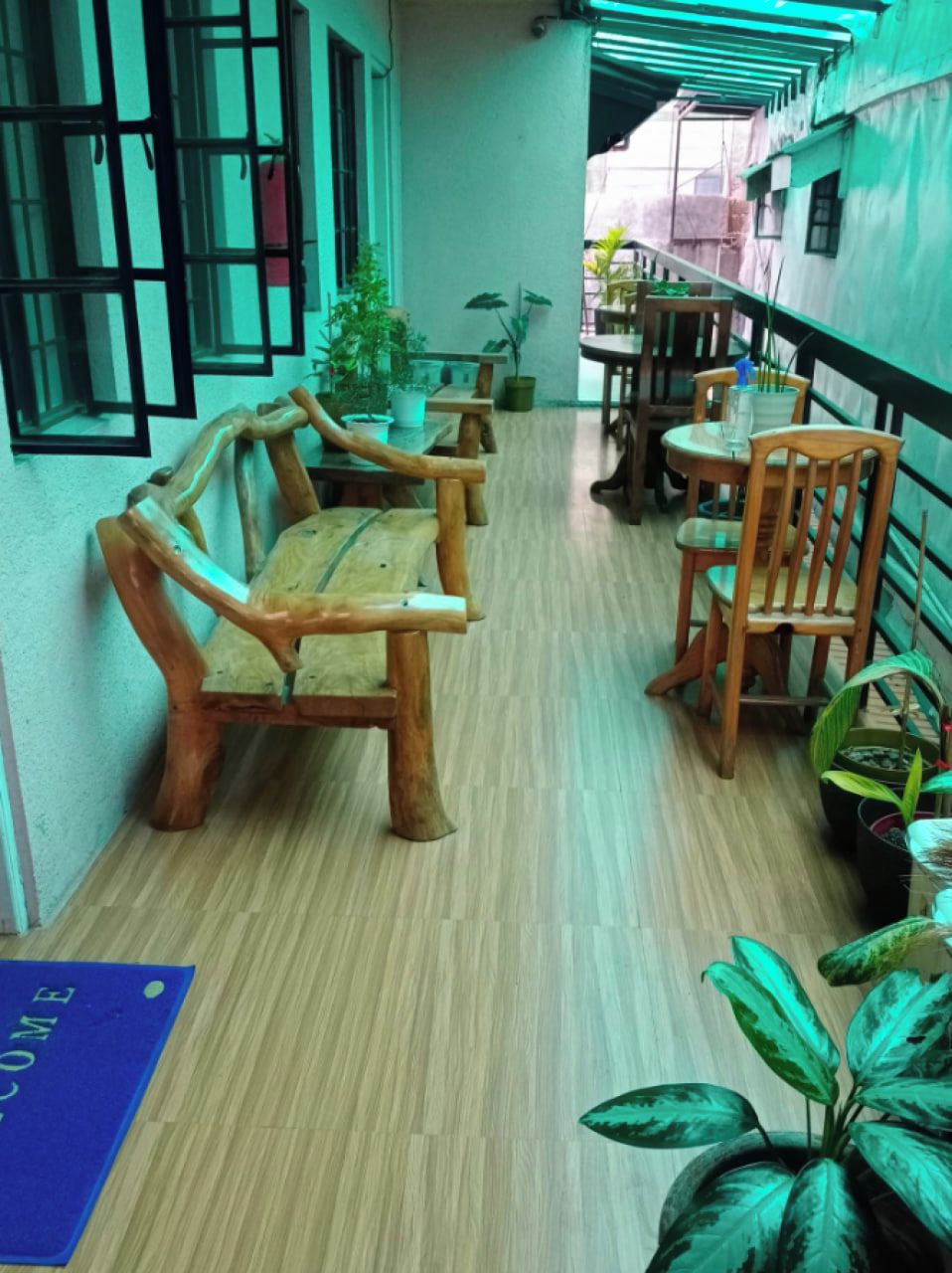 A corridor with wooden benches and tables, potted plants, and a blue mat on the floor.