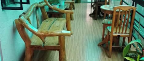 A corridor with wooden benches and tables, potted plants, and a blue mat on the floor.