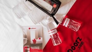 Une présentation promotionnelle comprenant une brochure RedDoorz, un sac en tissu noir et une bouteille d’eau, le tout disposé sur un fond en tissu blanc.