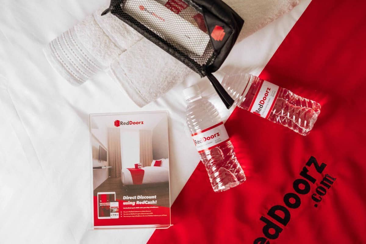 Un expositor promocional con un folleto de RedDoorz, una bolsa de malla negra y una botella de agua sobre un fondo blanco de tela.