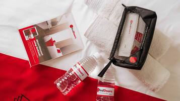 Eine Wasserflasche, ein Handtuch und eine Geldbörse mit RedDoorz-Logo auf einem Bett mit roter und weißer Bettdecke.