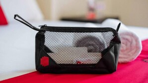 Un sac noir en filet muni d’une fermeture éclair et d’une étiquette rouge, posé sur une surface rouge.