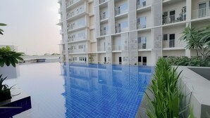 A modern building with a rooftop swimming pool, surrounded by greenery.