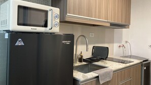A kitchen with a microwave on top of a black refrigerator, a sink with a faucet, and wooden cabinets.