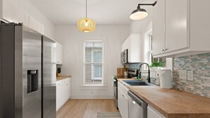 Una cocina moderna con electrodomésticos de acero inoxidable, encimera de madera y una lámpara colgante.