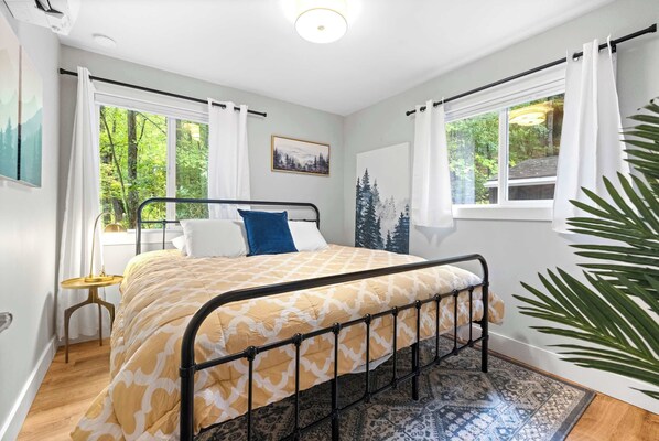 Un dormitorio con cama, una mesita y una ventana con cortinas.