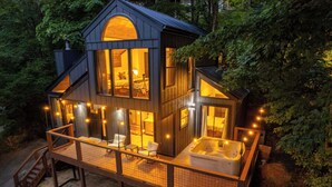 Una cabaña moderna con una amplia terraza, un jacuzzi y un interior acogedor con chimenea.