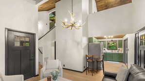 Amplia sala de estar con candelabro, un sofá, una mesa de centro con un libro, y una escalera que conduce a un nivel superior.