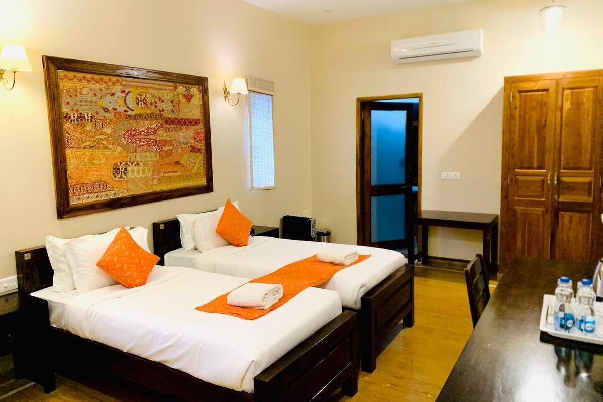 Habitación de hotel con dos camas, un gran tapiz decorativo, un equipo de aire acondicionado y un armario de madera.
