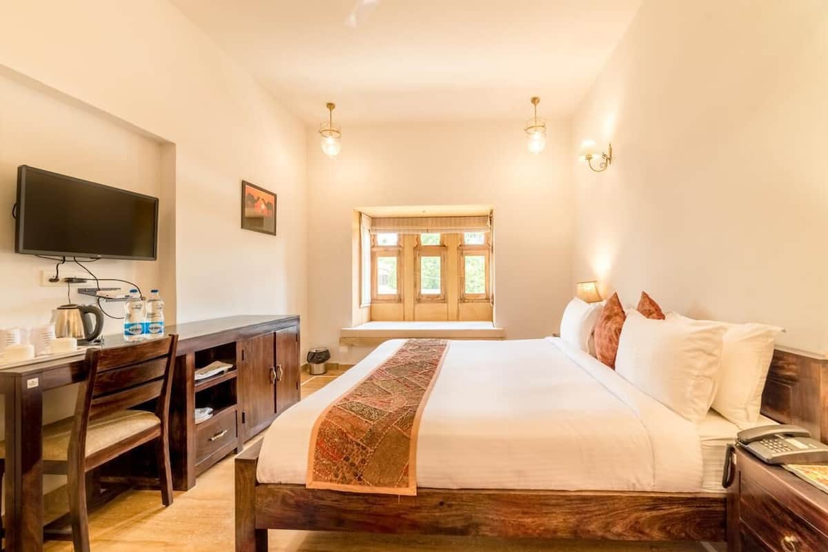 Habitación de hotel con cama, escritorio con televisor de pantalla plana, ventana con vista a follaje y lámpara de pared.