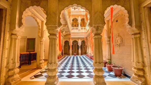 A corridor with ornate arches and a checkered floor, leading to a balcony with intricate ceiling designs. - Hotel Dev Villa (Jaisalmer)