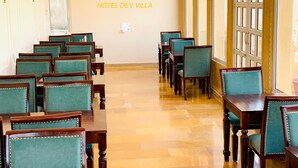 A restaurant with rows of green upholstered chairs and wooden tables, a tiled floor, and hanging pendant lights. - Hotel Dev Villa (Jaisalmer)