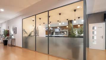 A modern hotel lobby with a reception desk, a coffee bar, and a large glass partition.