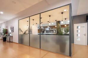 A modern hotel lobby with a reception desk, a coffee bar, and a large glass partition. - Alda Puerto Seco (Burgos)