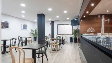 A modern restaurant with wooden and black chairs, a counter with a glass display, and a large window.