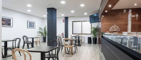 A modern restaurant with wooden and black chairs, a counter with a glass display, and a large window.