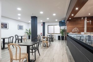 Un restaurant moderne avec des chaises en bois et noires, un comptoir doté d’une vitrine et une grande fenêtre.