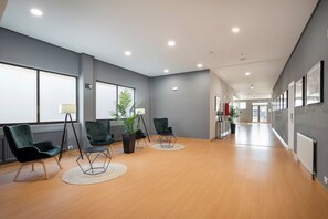 A spacious hallway with wooden flooring, green upholstered chairs, and a potted plant. - Alda Puerto Seco (Burgos)