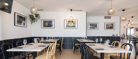 Un restaurante moderno con mesas largas, sillas negras de madera e iluminación colgante.